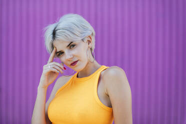 Beautiful blond woman standing in front of purple wall, portrait - TCEF00741