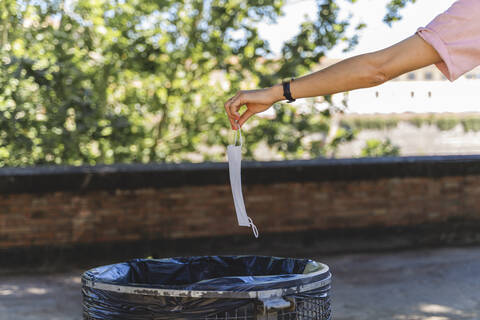 Hand of woman holding protective mask over garbage bin in city stock photo