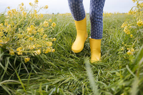 Grl's Beine in gelben Gummistiefeln auf Rapsfeld, lizenzfreies Stockfoto