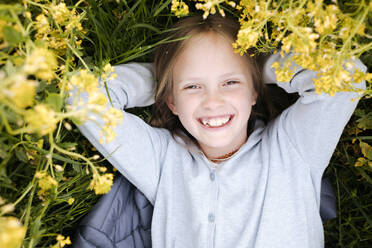 Smiling girl lying in rape flowers - EYAF01129