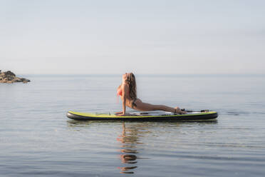 Woman practicing upward facing dog position on paddleboard over sea against sky - DLTSF00758