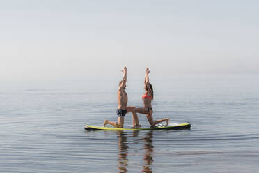 Paar übt gemeinsam Yoga auf einem Paddelbrett über dem Meer - DLTSF00762