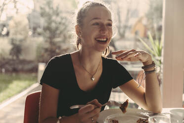 Glückliches Mädchen im Teenageralter genießt das Frühstück, während sie zu Hause wegschaut - MFF05889