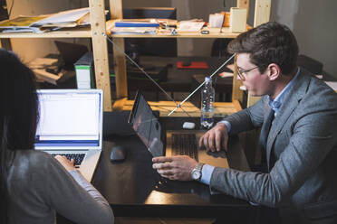 Geschäftsmann und Frau verwenden Laptops am Schreibtisch im Büro - MEUF00817
