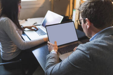 Geschäftsmann und Frau verwenden Laptops am Schreibtisch im Büro - MEUF00818