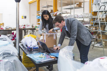 Geschäftsmann mit Laptop und Mitarbeiterin beim Verpacken von Waren in einem Lagerhaus - MEUF00832