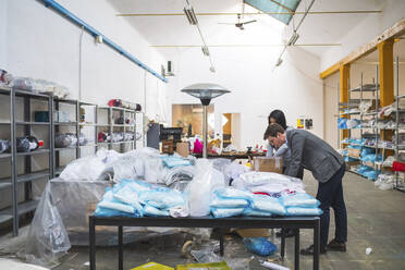 Businessman using laptop and female employee packing merchandise in a warehouse - MEUF00834