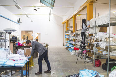 Businessman with laptop and female employee on step ladder in a warehouse - MEUF00835