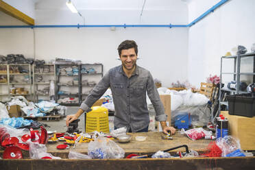 Portrait of smiling man at workbench with fencing supplies - MEUF00873