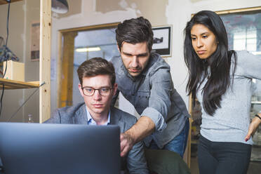 Three business people sharing laptop at desk in office - MEUF00887