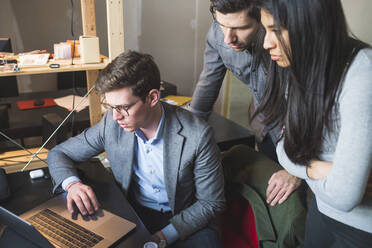 Three business people sharing laptop at desk in office - MEUF00888