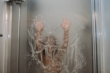 Kind spielt mit Seife an der Duschtür mit den Händen - CAVF85095