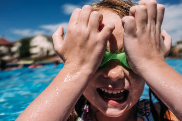 Nahaufnahme eines kleinen Kindes, das sich am Pool eine Schwimmbrille aufs Gesicht drückt - CAVF85106