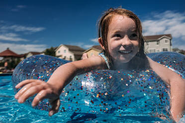 Nahaufnahme eines jungen Mädchens, das auf einem runden Schwimmer im Pool schwimmt - CAVF85107