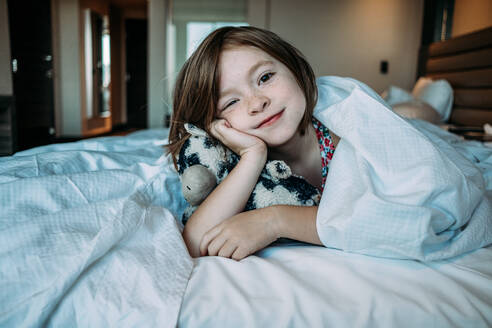 Straight on of young girl laying in a bed with her stuffed animal - CAVF85109