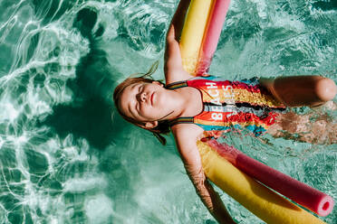 Young girl floating on her back in pool with eyes closed - CAVF85115