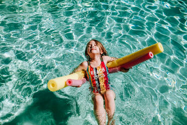 Young girl swimming on her back in pool with eyes closes - CAVF85116