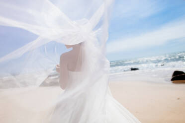 Rückansicht der Braut im Kleid stehend am Strand - EYF05499