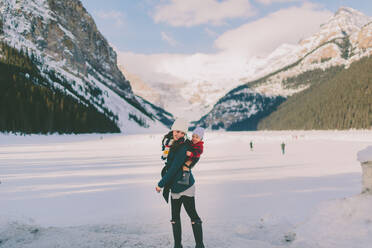 Mutter nimmt Sohn im Huckepack auf Schnee gegen Berge im Winter - EYF05504