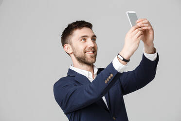 Geschäftsmann, der ein Selfie mit seinem Smartphone macht, während er vor einem grauen Hintergrund steht - EYF05510
