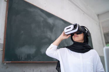 Lächelnde junge Frau nutzt virtuelle Realität im Klassenzimmer - EYF05555