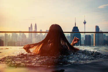 Rückansicht der Frau Schwimmen im Infinity Pool in der Stadt - EYF05557