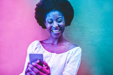 Cheerful Young Woman Using Mobile Phone Against Wall - EYF05577