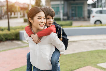 Happy Mother Piggybacking Schoolboy While Walking On Footpath - EYF05592