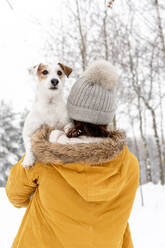 Rear View Of Woman In Warm Clothing Carrying Dog In Snow Covered Forest - EYF05597