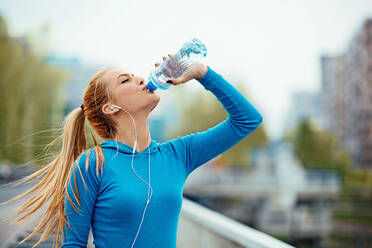 Sporty Young Woman Drinking Water On Bridge - EYF05599