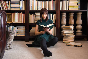 Young Woman Reading Book While Sitting Against Bookshelf In Library - EYF05645