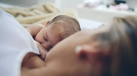 High Angle View Of Mother Breastfeeding Daughter While Lying On Bed At Home - EYF05647