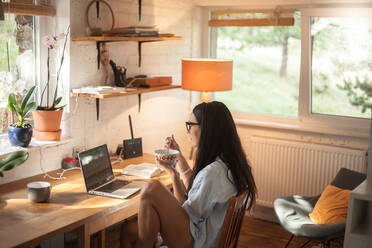 Woman Eating Food While Using Laptop On Table At Home - EYF05653