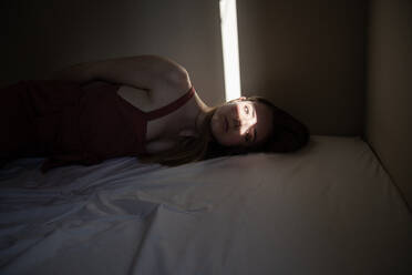 Woman lying down on floor relaxing in sunlight at home stock photo