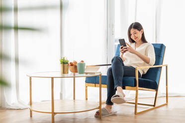 Woman Using Phone While Sitting On Chair By Breakfast On Table - EYF05702