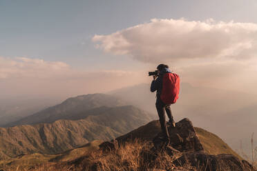 Man Photographing While Standing On Mountain Against Sky - EYF05714