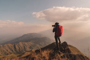 Mann beim Fotografieren auf einem Berg gegen den Himmel stehend - EYF05714