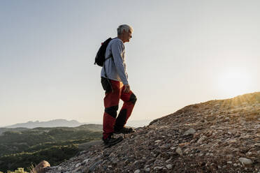 Active senior man hiking up on mountain against sky - AFVF06666