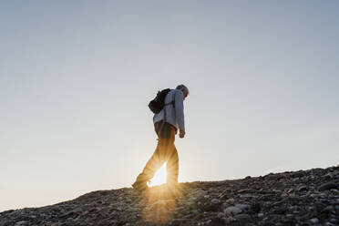 Sonnenstrahl durch aktiven älteren Mann beim Wandern auf einem Berg gegen den Himmel - AFVF06667