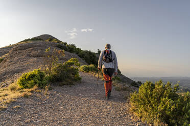 Aktiver älterer Mann mit Wanderstock auf einem Berg bei Sonnenuntergang - AFVF06671