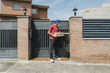 Männlicher Postbeamter benutzt die Gegensprechanlage, während er mit einem Paket an der Haustür steht - XLGF00185