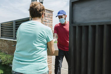 Senior woman receiving delivery package from postal worker at gate - XLGF00191