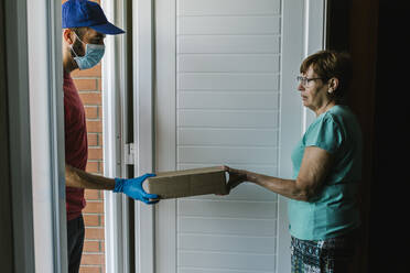 Postal worker delivering package to senior woman at doorway during coronavirus - XLGF00196