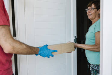 Smiling senior woman receiving package from delivery person at doorway - XLGF00197