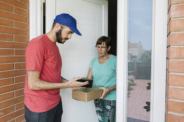 Postangestellte zeigt einer älteren Frau an der Tür ein digitales Tablet zur Unterschrift - XLGF00200