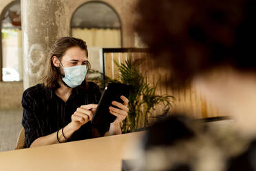 Young man wearing mask while sitting and using digital tablet in restaurant - EGAF00202