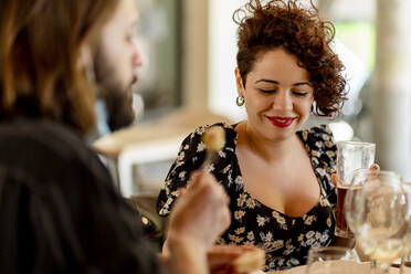 Schöne junge Frau mit lockigen braunen Haaren sitzt mit Freund im Restaurant - EGAF00227