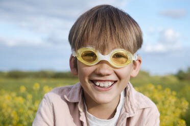 Blonder Junge mit Schwimmbrille auf einem Rapsfeld an einem sonnigen Tag - EYAF01144