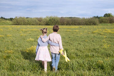 Boy holding toy airplane while standing with arm around sister on rape field - EYAF01146