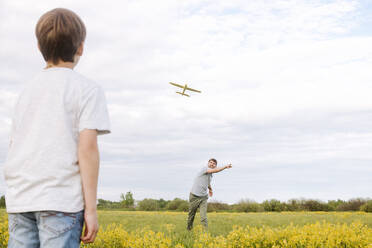 Father and son playing with toy airplane on rape field against sky - EYAF01149